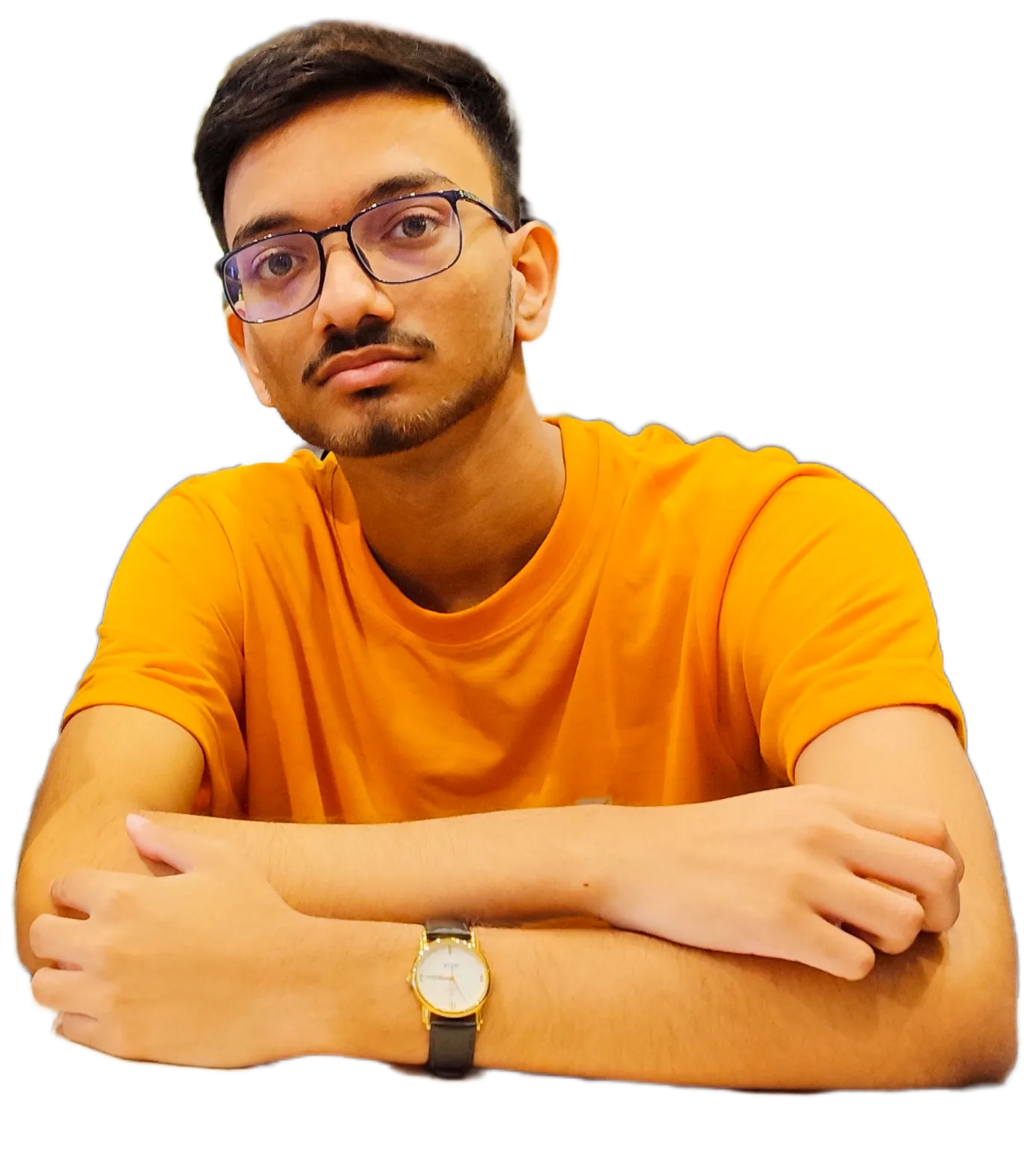 Suprava Dutta in an orange t-shirt, arms folded on a table, wearing glasses and a gold wristwatch